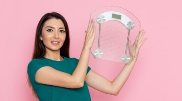 A woman holding up a weighing scale following weight gain