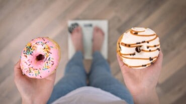 A woman holding two donuts, standing on a weighing scale